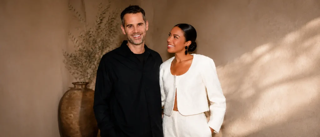 Swedish fashion entrepreneur Jens Grede standing next to his wife, British businesswoman Emma Grede, smiling together in matching premium black and white outfits.