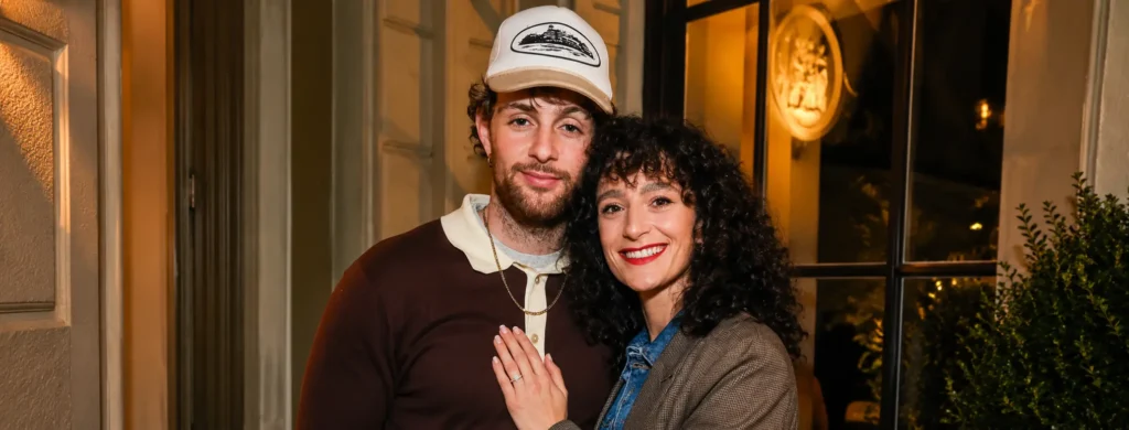 British singer Tom Grennan and his wife, Danniella Carraturo, smiling together at an evening event, with Danniella displaying her ring.